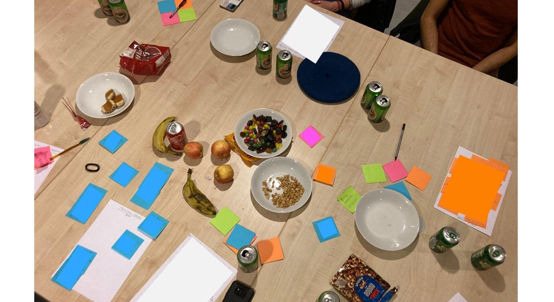 A picture showing chaotic post-it notes, fruit, candy and cans on a wooden table